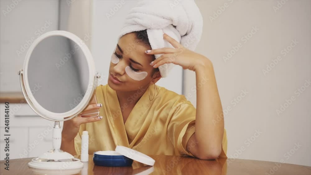 Closeup portrait of beautiful woman after bath with towel on head puts patches under the eyes from wrinkles and dark circles. Attractive female in bathrobe makes beauty treatments on the face at home. Closeup portrait of beautiful woman after bath with towel on head puts patches under the eyes from wrinkles and dark circles. Attractive female in bathrobe makes beauty treatments on the face at home.
