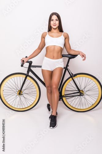 Fototapeta Naklejka Na Ścianę i Meble -  Full length portrait of a smiling woman in sportwear standing near bicycle on gray background