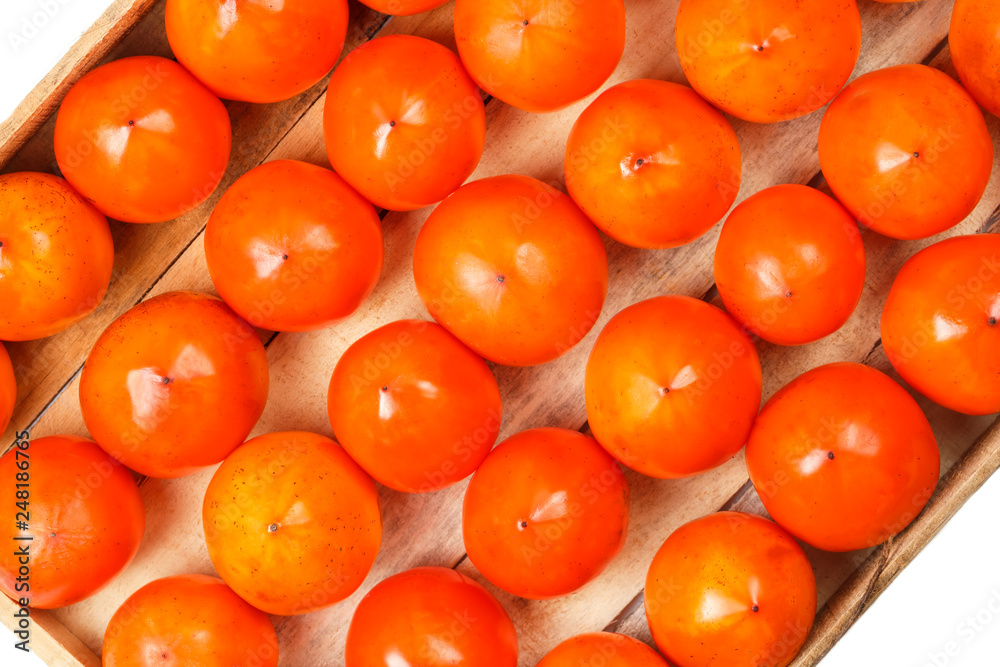 Juicy ripe persimmon in a large wooden box on a white background.