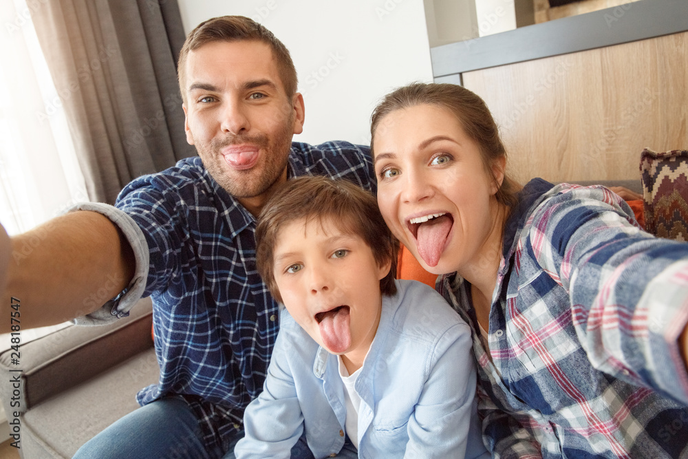 Family at home sitting on couch in living room together taking selfie pictures tongue out playful Family at home sitting on couch in living room together taking selfie pictures tongue out playful
