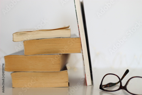Books with vintage glasses on a white table.
