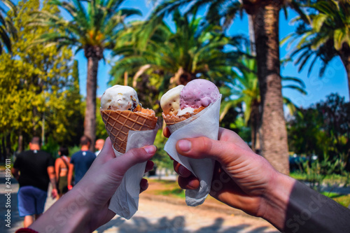 A couple or friends are holding an ice cream cones in their hands outdoor. Summer activity, palm trees on the background.
