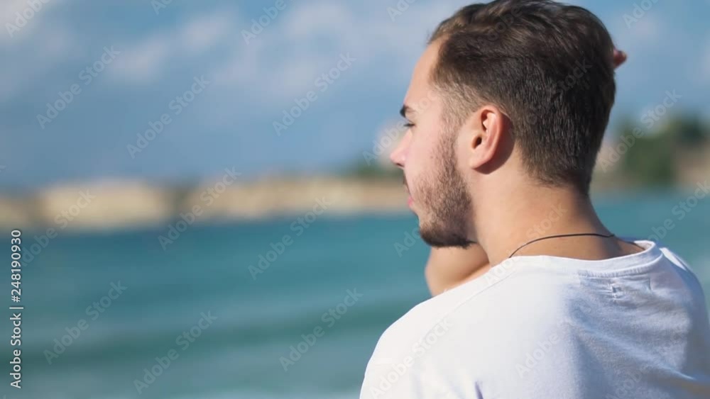 Close up profile portrait of handsome young man straightening his hair and focused on looking on sea on seaside background Close up profile portrait of handsome young man straightening his hair and focused on looking on sea on seaside background