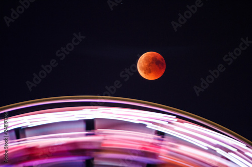 Mondfinsternis über einem sich drehenden Riesenrad photo