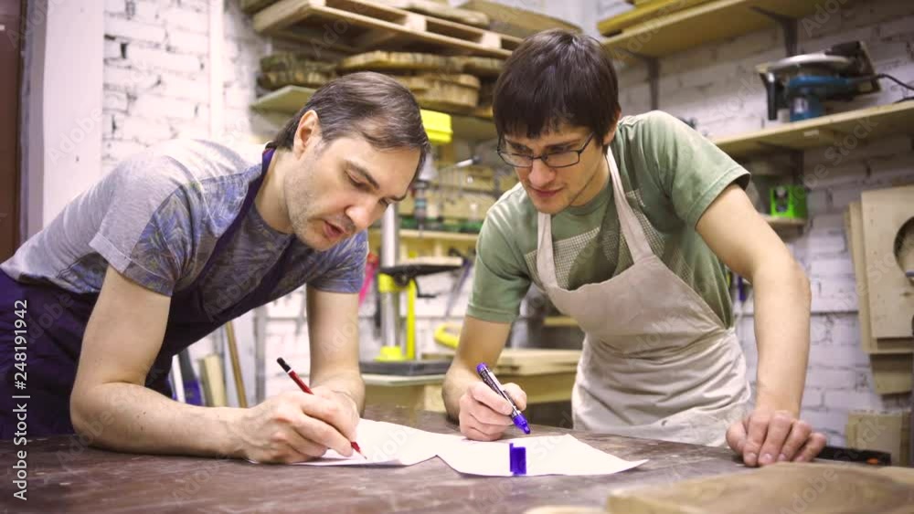 Two carpenters discuss drawing (round wood) in the workshop Two carpenters discuss drawing (round wood) in the workshop