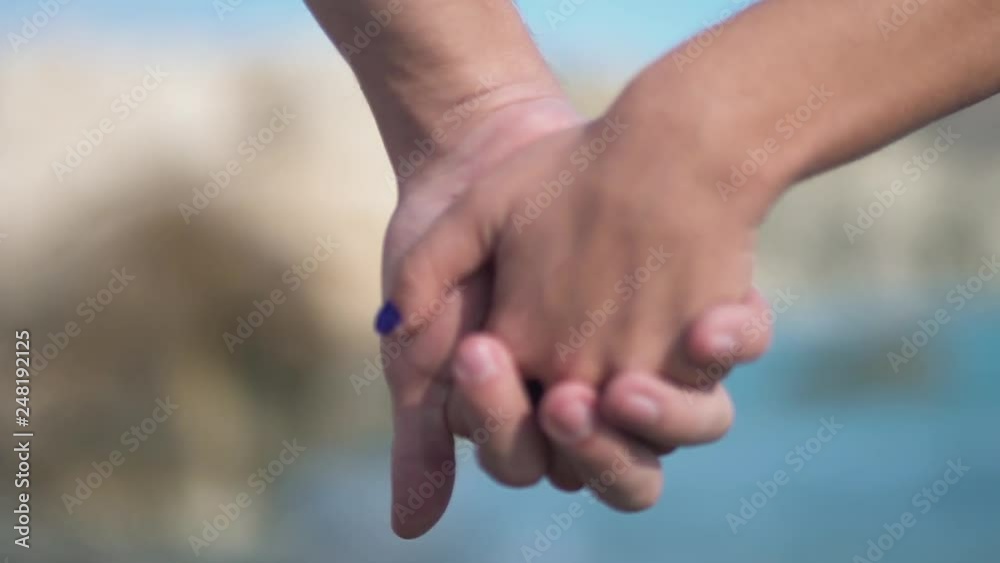Close up backs of charming couple holding hands and walking in the sunny beach. Union, caring for a partner. Slow motion.