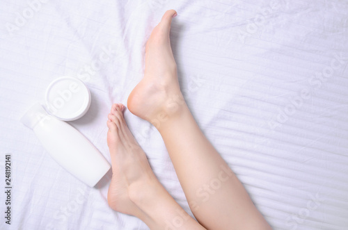 Female legs feet heel foot white jar cream in white bed, top view