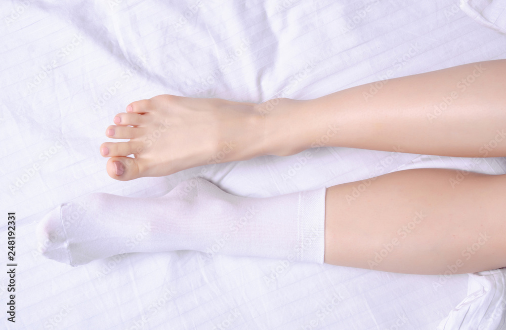 Female legs in white socks in white linens bed, top view Stock Photo