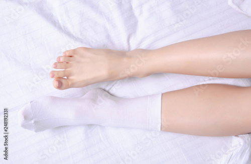 Female legs in white socks in white linens bed, top view