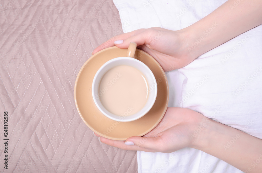 Woman holding cup of coffee in the white linens bed brown blanket, top view Woman holding cup of coffee in the white linens bed brown blanket, top view