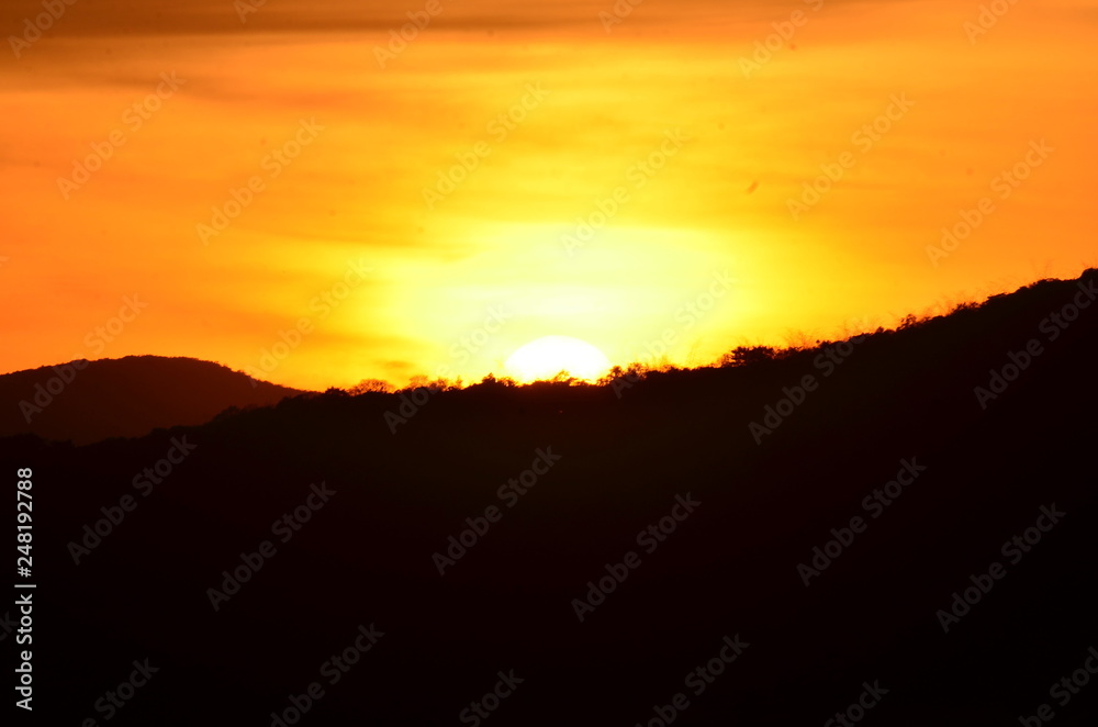Sunset in the mountains.Picture of a sun setting behind a dense forest area followed by mountains.	