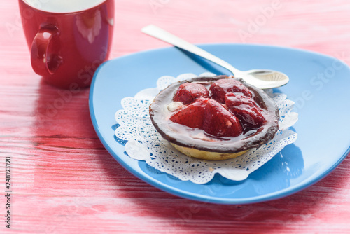 A cupcake with a strawberry, next to coffee in a cup, photographed on a wooden background.