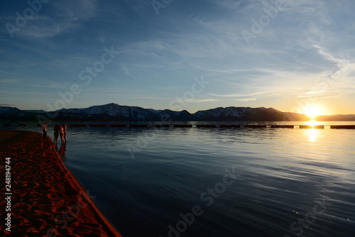 sunset on the lake with group of people on the beach 