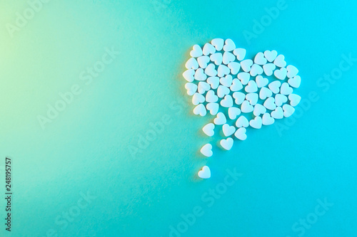 White heart shaped candies on a blue paper background. Dripping heart or pearts gethering love concept.