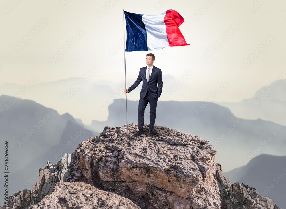 Obraz premium Successful businessman on the top of a mountain holding France victory flag 