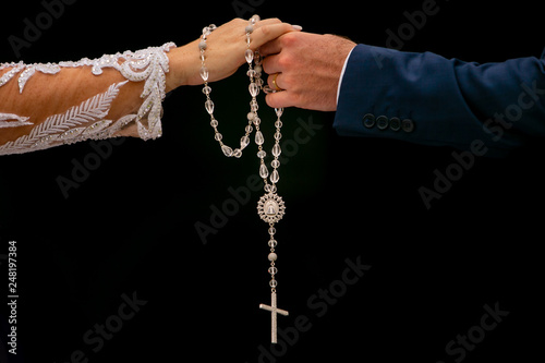 Mãos de uma mulher e um homem, noivos, segurando um terço com crucifixo em fundo preto