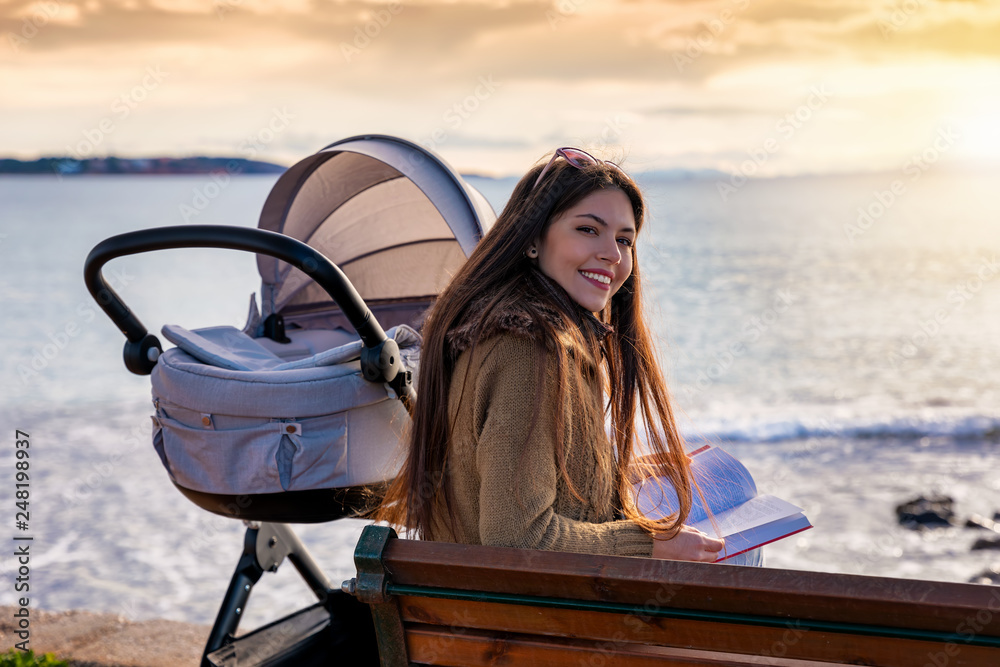 Portrait einer jungen Mutter mit ihrem Baby im Kinderwagen die am Strand  ein Buch liest und entspannt – Stock-Foto | Adobe Stock