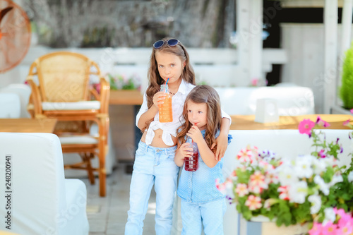 Friendly kid girl and fun emotional mother drinking berries smoothie juice together in street cafe and looking on each other. Closeup portrait