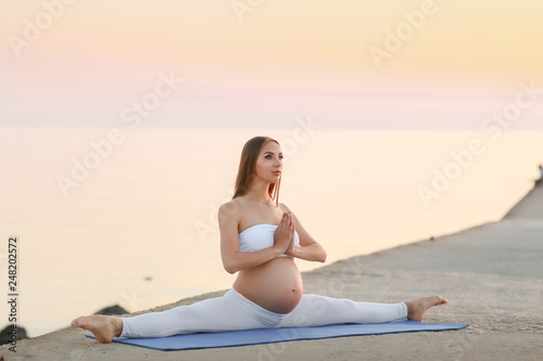Beautiful pregnant woman doing yoga at the sea side