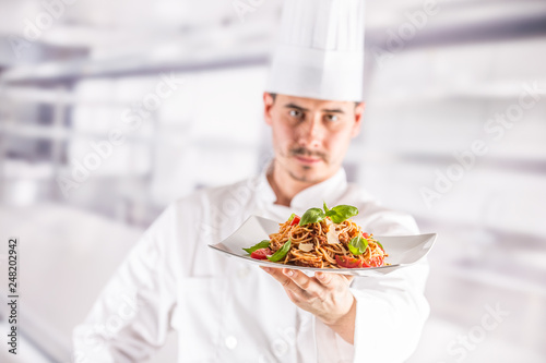 Chef in restaurant kitchen holding plate with italian meal spagh