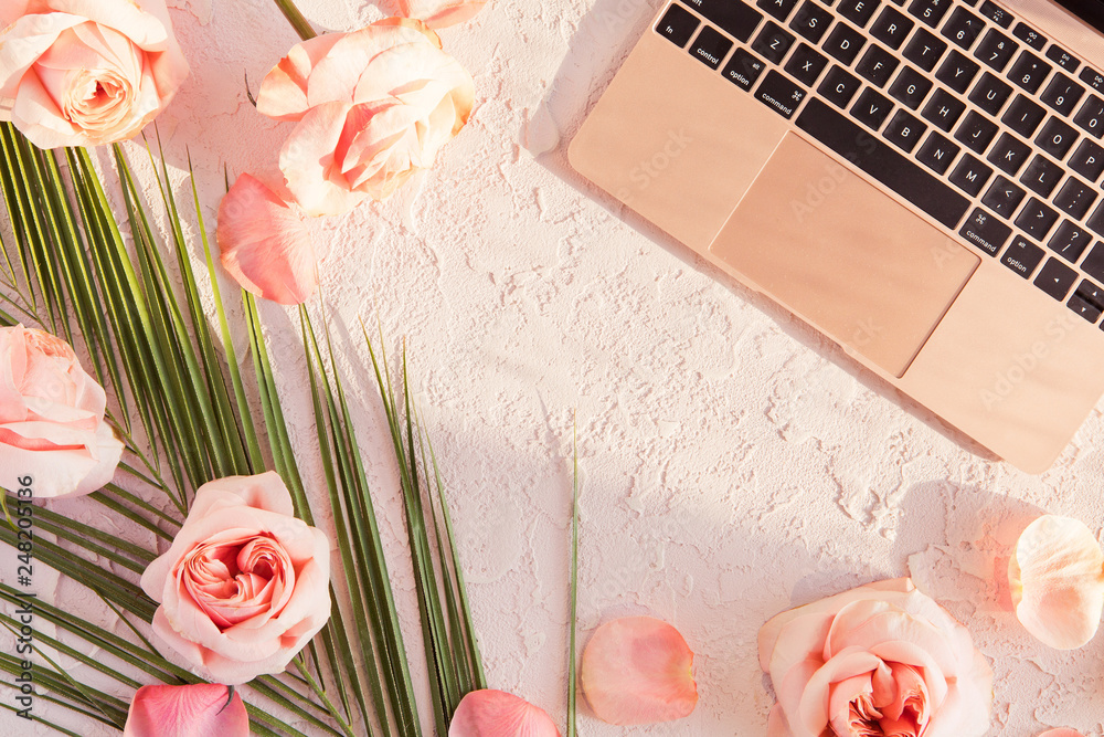 Flat lay of stylish composition with tropical palm leaf, pink rose flowers,  on pastel background with shadows and sun light. Top view of feminine rose  gold desk with laptop Stock Photo