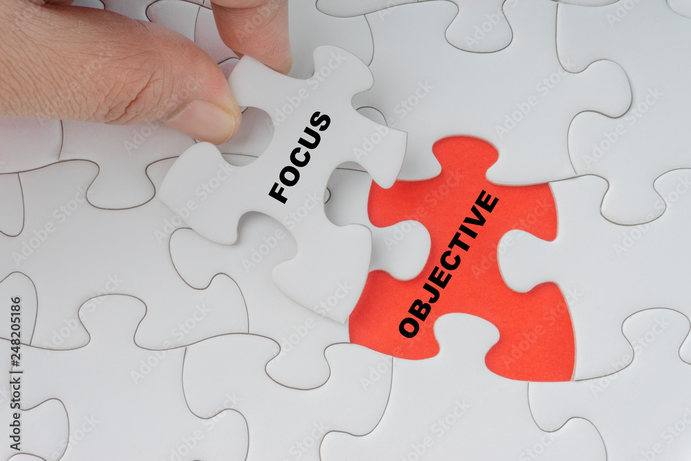 Hand holding piece of jigsaw puzzle with word FOCUS OBJECTIVE. Selective focus Hand holding piece of jigsaw puzzle with word FOCUS OBJECTIVE. Selective focus
