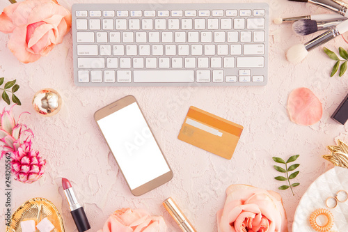 Top view of credit card and mobile phone with blank screen, online shopping and payment concept, female pastel pink workspace with flowers and laptop, flat lay.