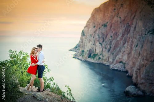 Happy young family pregnant pretty girl with husband on the cliff in mountains over sunset lights