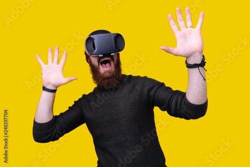 Scared shocked bearded man having virtual reality headset experience with open mouth on yellow background
