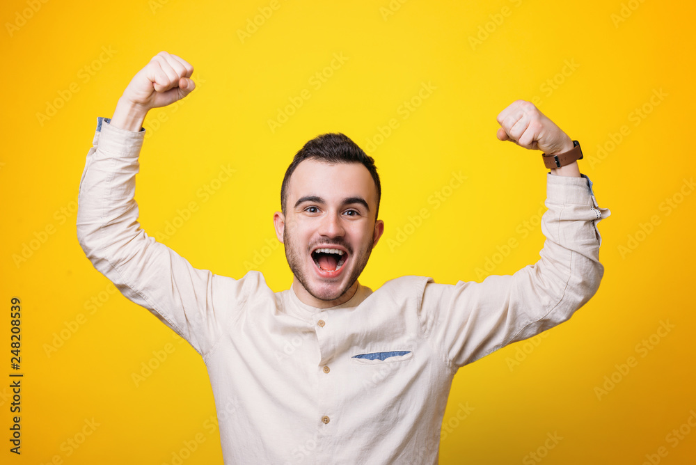 Naklejka premium Portrait of a satisfied young man celebrating success with haraised hands over yellow background