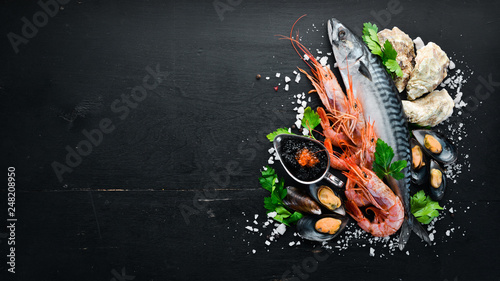 Seafood. Fresh fish, shrimp, oysters and caviar on a black wooden background. Top view. Free copy space.