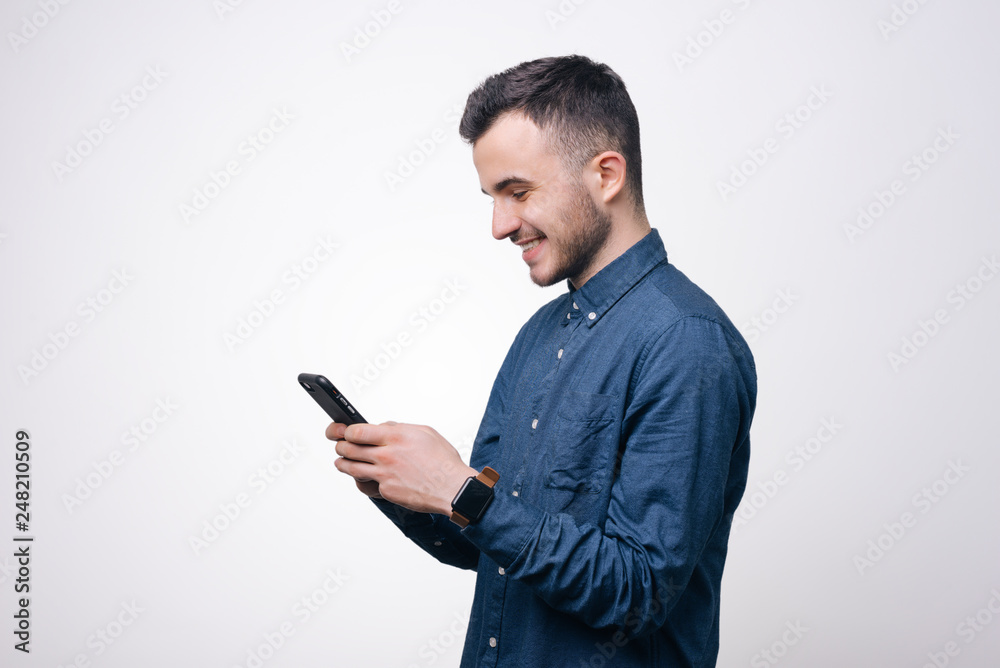 Smart casual ypung man in blue shirt using smartphone in studio over white background Smart casual ypung man in blue shirt using smartphone in studio over white background