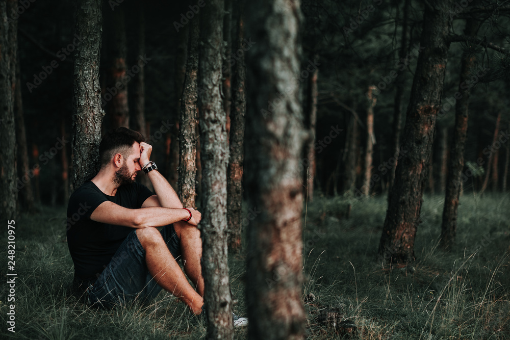 Young depressed man sitting alone in the forest