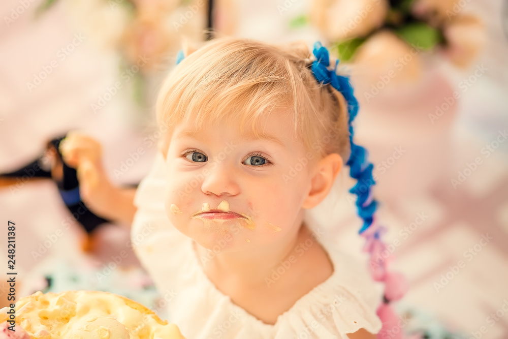 Portrait of a little cheerful birthday girl with the first cake. Eating the first cake. Smash cake. Portrait of a little cheerful birthday girl with the first cake. Eating the first cake. Smash cake.