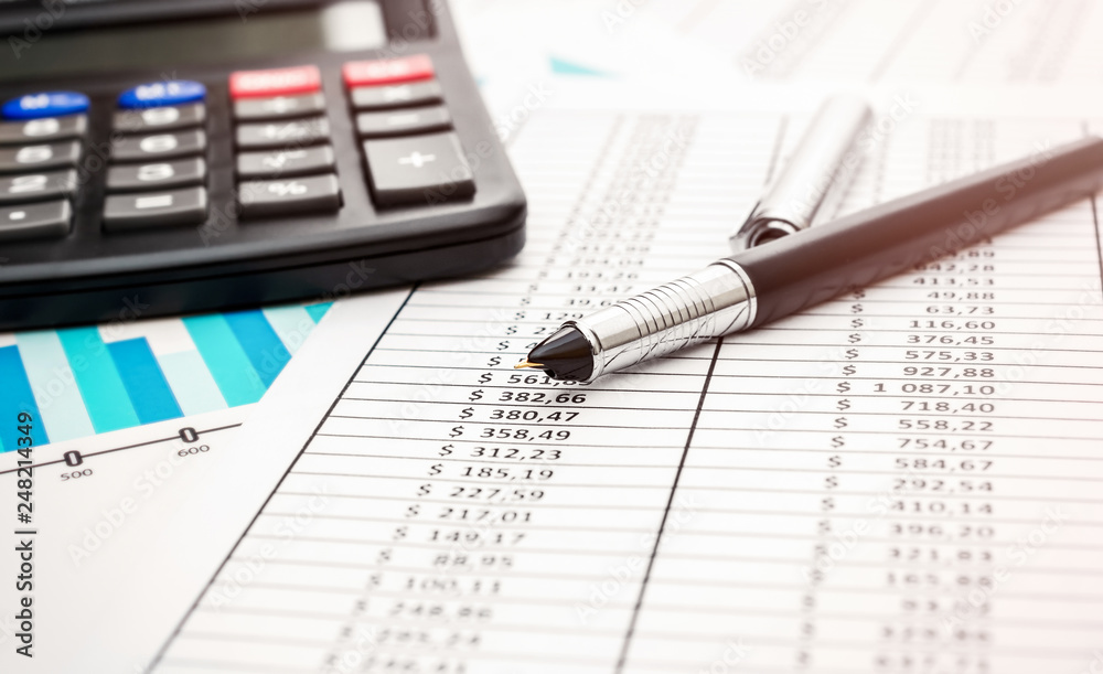 Pen with calculator on financial graph and documents. Toned image. Pen with calculator on financial graph and documents. Toned image.