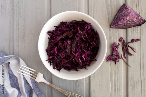 Salad with blue cabbage in the white plate on the grey wooden background.Top view.