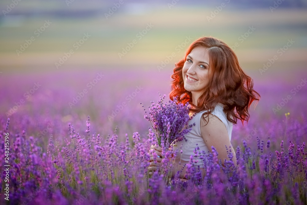 Redhead young woman in brightly summer dress looking out onto the fields of lavender on the plateau of Valensole, France. Redhead young woman in brightly summer dress looking out onto the fields of lavender on the plateau of Valensole, France.