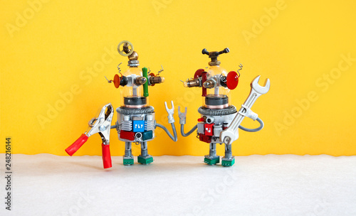 Maintenance repair service concept. Two comical electrician robots are ready for maintenance. Robotic toy handymans red pliers hand wrench on yellow gray background.