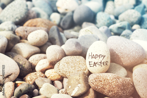 Easter egg from a stone with the inscription Happy Easter on the sea pebble beach, toned. Easter background