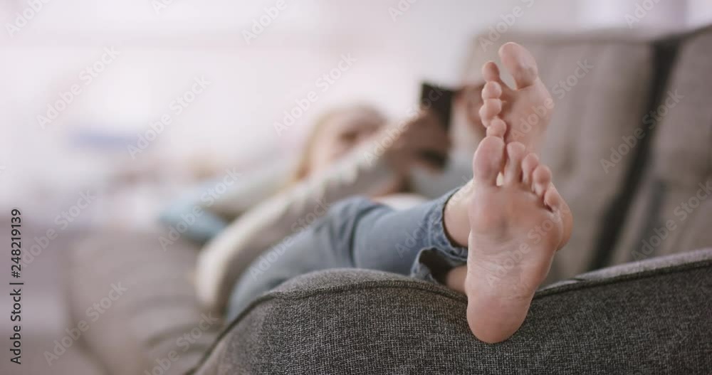 Young attractive woman stretches her bare feet on the couch while using her mobile phone