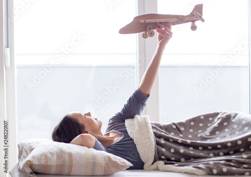 Girl in bed holding airplane toy and daydreaming
