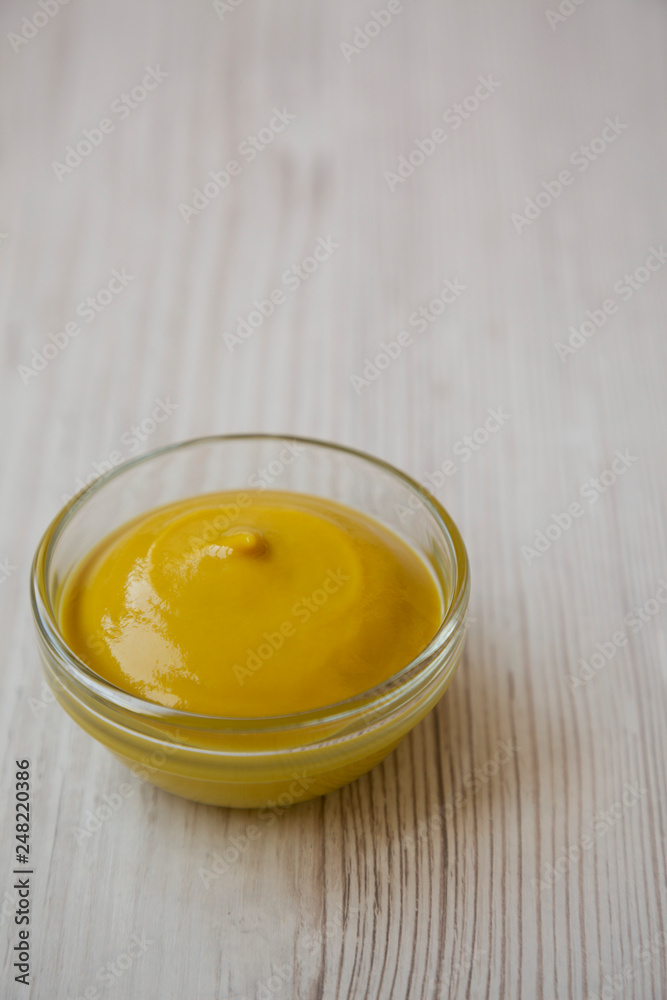 Homemade organic mustard in glass bowl on white wooden background, low angle view. Copy space.