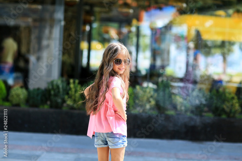 Fashion kid summer in the city stands on a streetl. Trendy girl in sunglasses standing on the street at sunset. photo