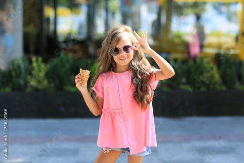 Fashion kid summer in the city stands on a streetl. Trendy girl in sunglasses standing on the street at sunset. photo