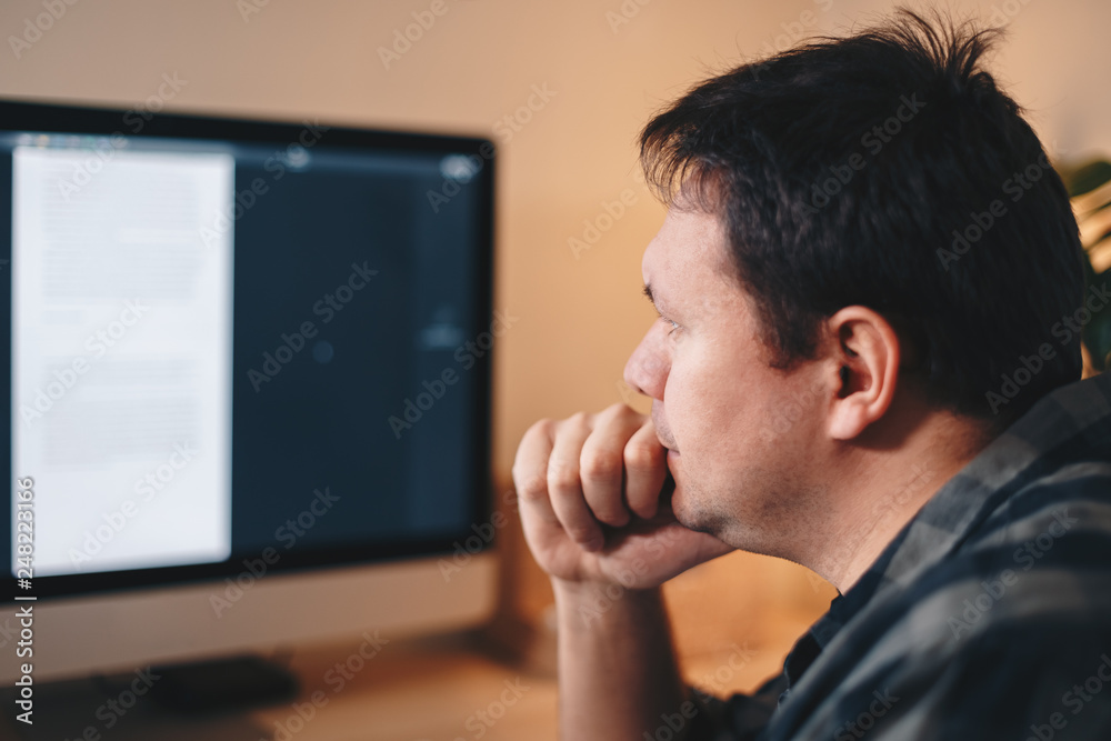 Young male freelancer being thoughtful while looking at the computer screen, working from home office. Concept of trouble solving. Young male freelancer being thoughtful while looking at the computer screen, working from home office. Concept of trouble solving.