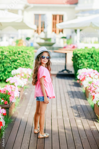 Fashion little girl model wearing a pink checkered shirt, hat and sunglasses in city