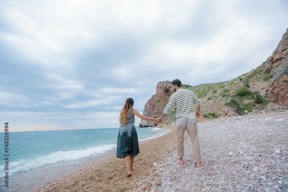 Romantic atmosphere. Happy couple woman and man walking the dog near the sea with mountains in the background.
