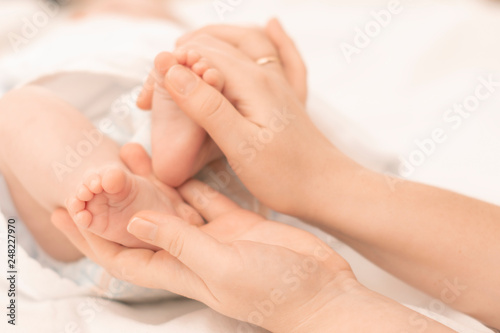 mother's hands gently hold the feet of a newborn baby in the palms © leksann