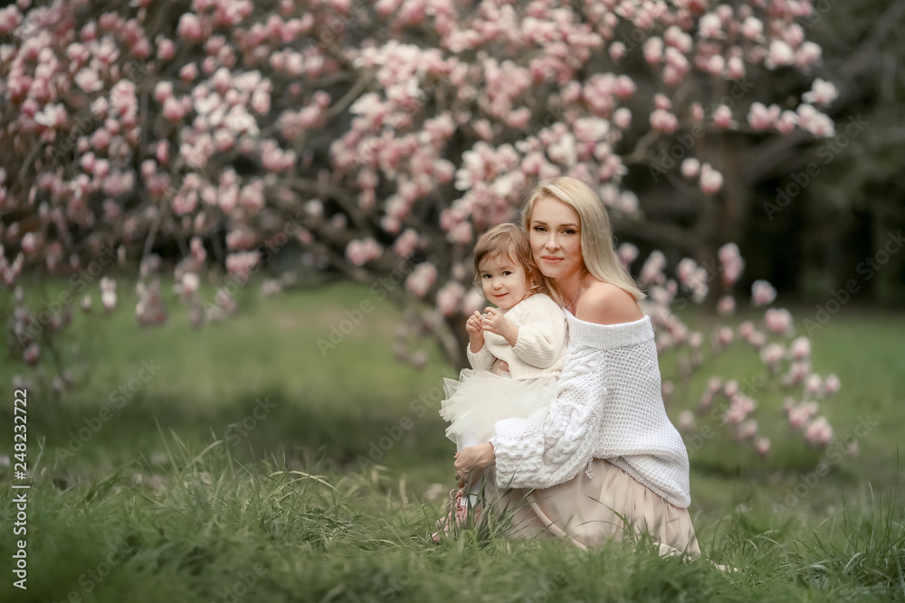 Portrait of happy joyful child in white clothes over tree flowers blossom background. Family playing together outside. Mom cheerfully hold little daughter Newborn spring concept Portrait of happy joyful child in white clothes over tree flowers blossom background. Family playing together outside. Mom cheerfully hold little daughter Newborn spring concept