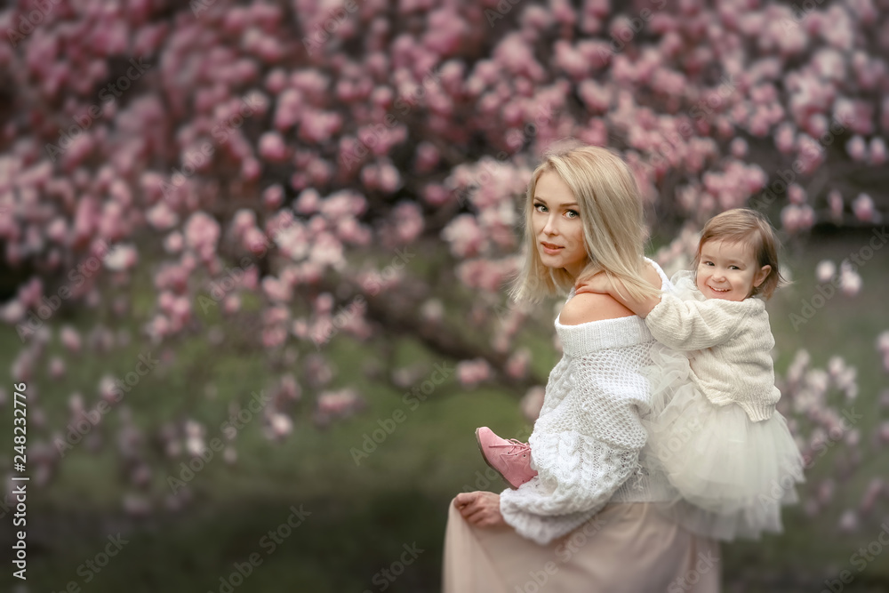 Portrait of happy joyful child in white clothes over tree flowers blossom background. Family playing together outside. Mom cheerfully hold little daughter Newborn spring concept Portrait of happy joyful child in white clothes over tree flowers blossom background. Family playing together outside. Mom cheerfully hold little daughter Newborn spring concept
